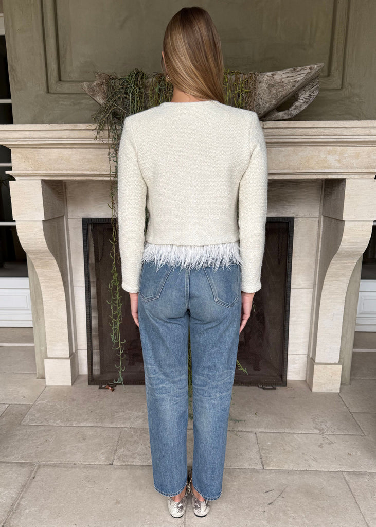 Person wearing a light-colored sweater and blue jeans standing in front of a fireplace.