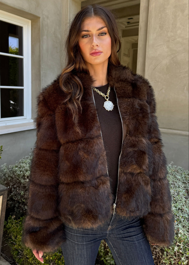 Woman wearing a brown fur coat standing outside a building.