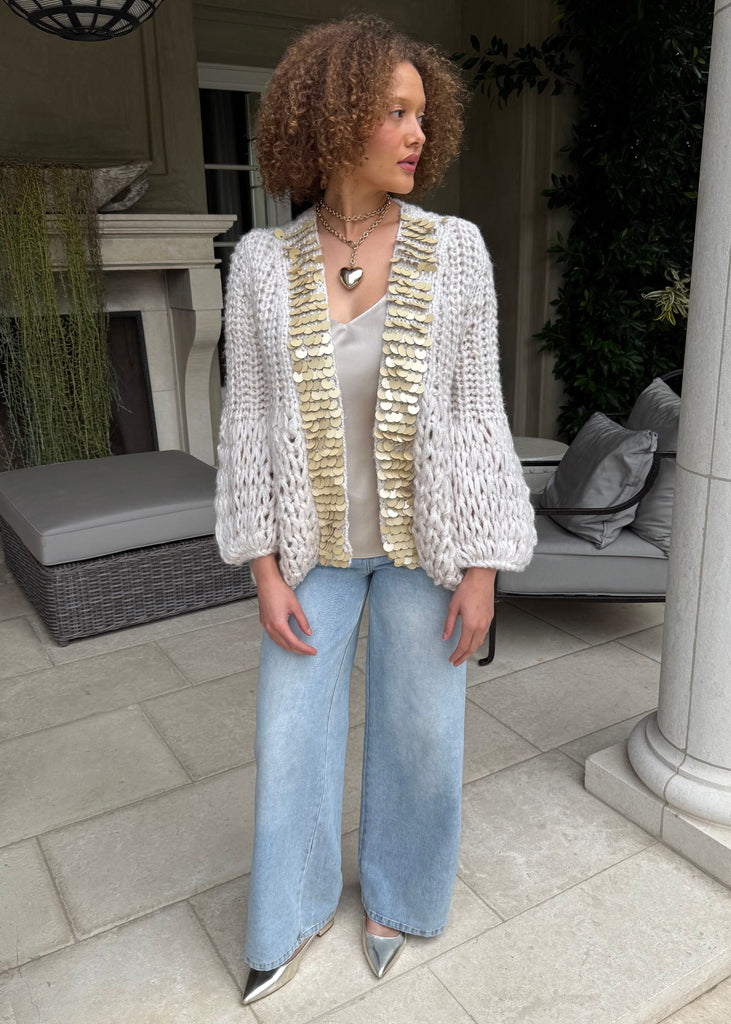 Woman wearing a textured cardigan, white top, and light blue jeans outdoors.
