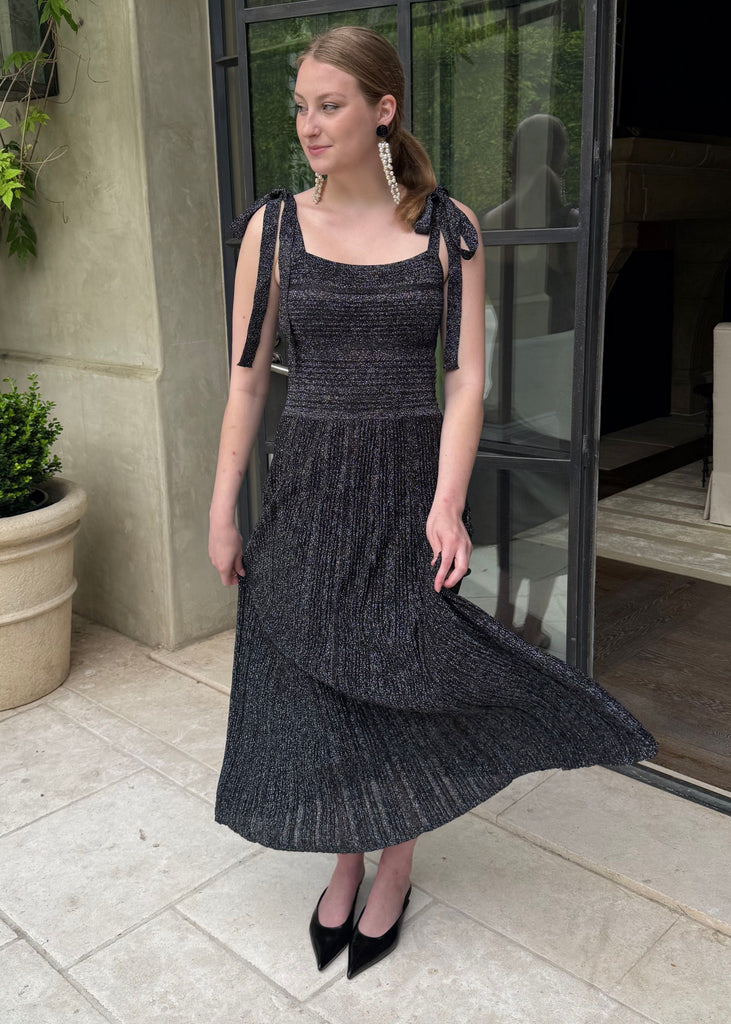 Woman in a black dress standing outdoors near a building entrance.