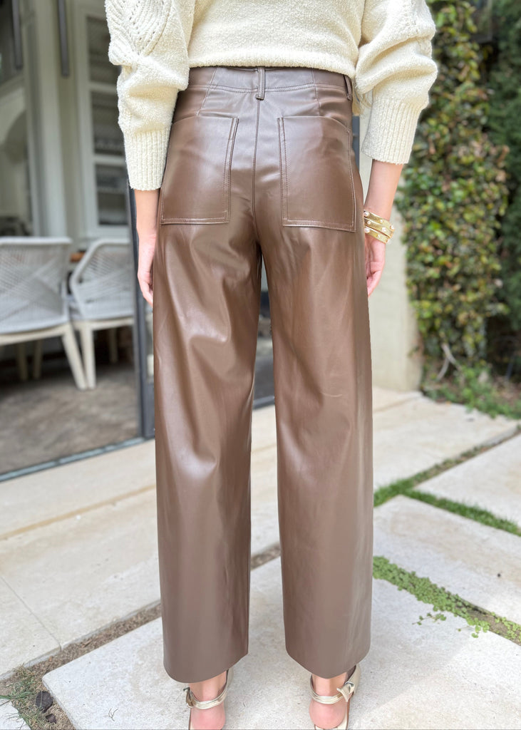 Person wearing a cream sweater and brown leather pants standing outdoors.