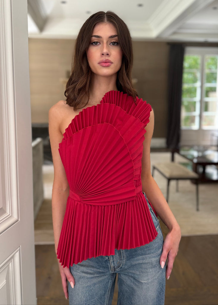 Woman wearing a red one-shoulder top and blue jeans in an indoor setting