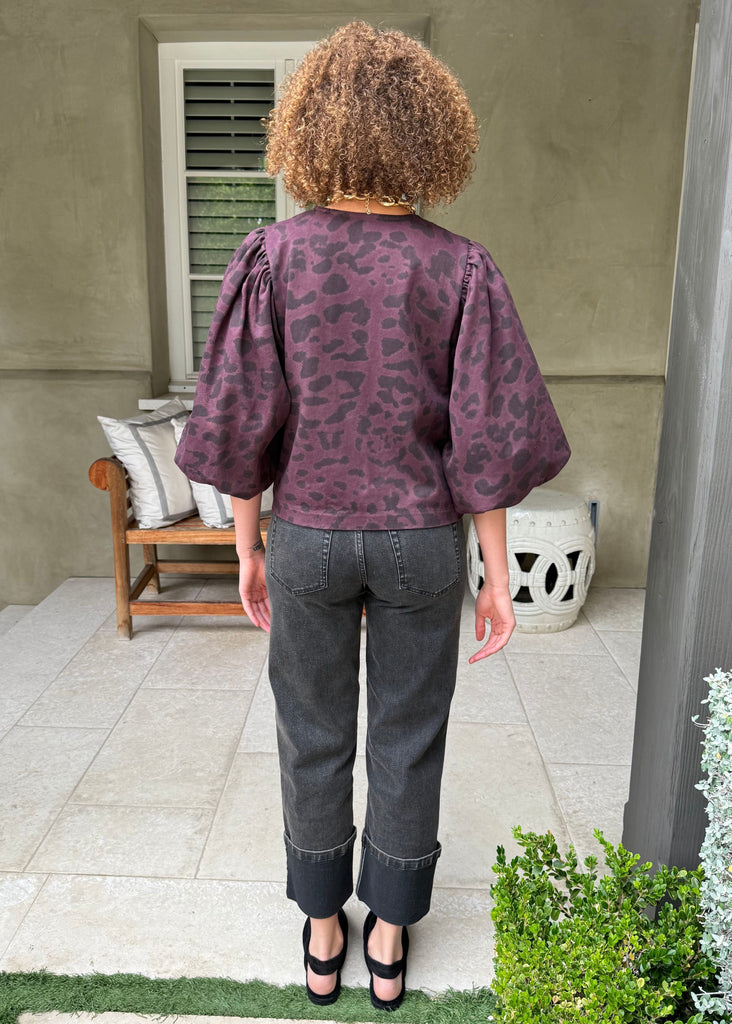 Person wearing a patterned top and dark jeans standing on a patio.