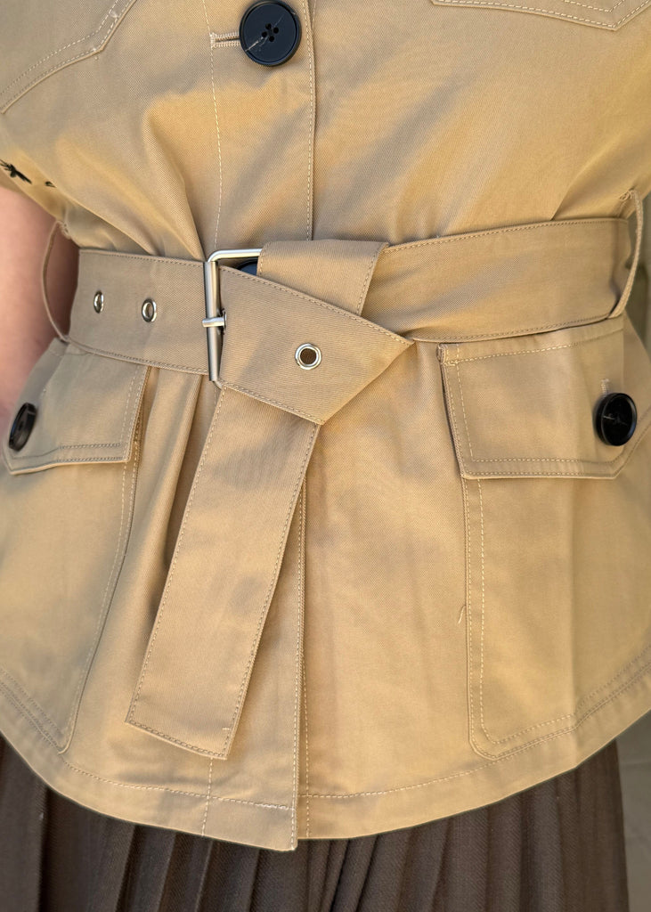 Close-up of a beige trench coat with a belt and button details.