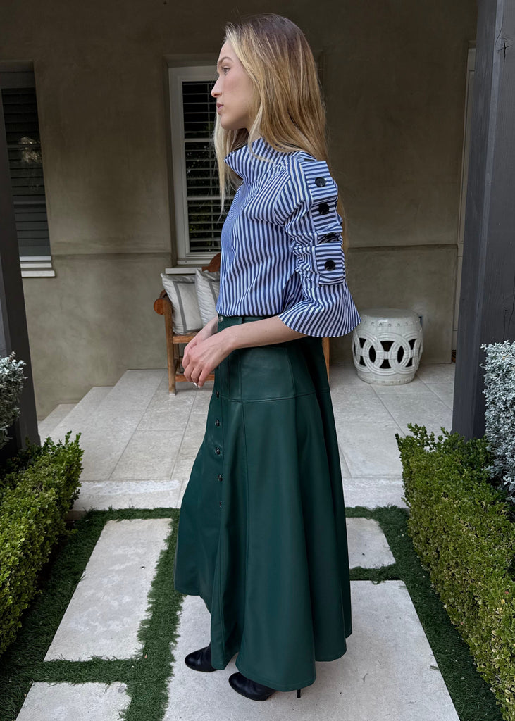 Woman in a blue top and green skirt standing in a garden setting.