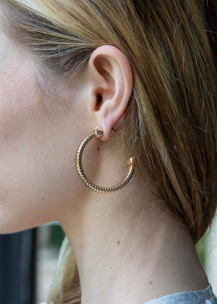 Close-up of a person wearing gold hoop earrings with a blurred background