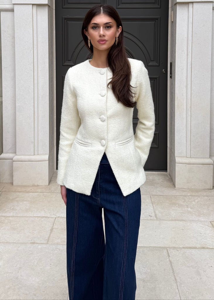 Woman in a white blazer and blue pants standing in front of a decorative archway.