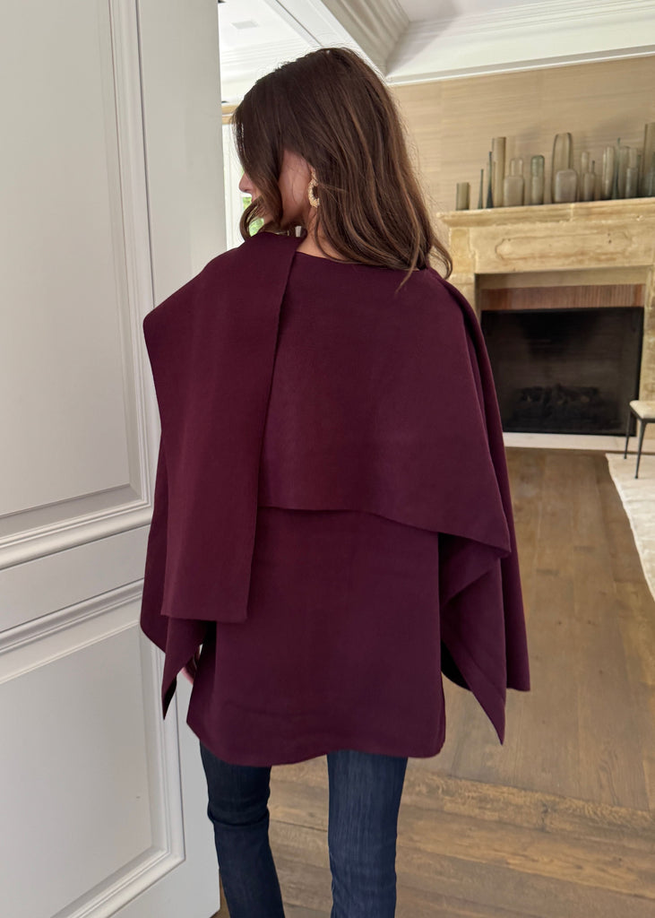 Person wearing a burgundy cape in a room with wooden flooring and a fireplace.