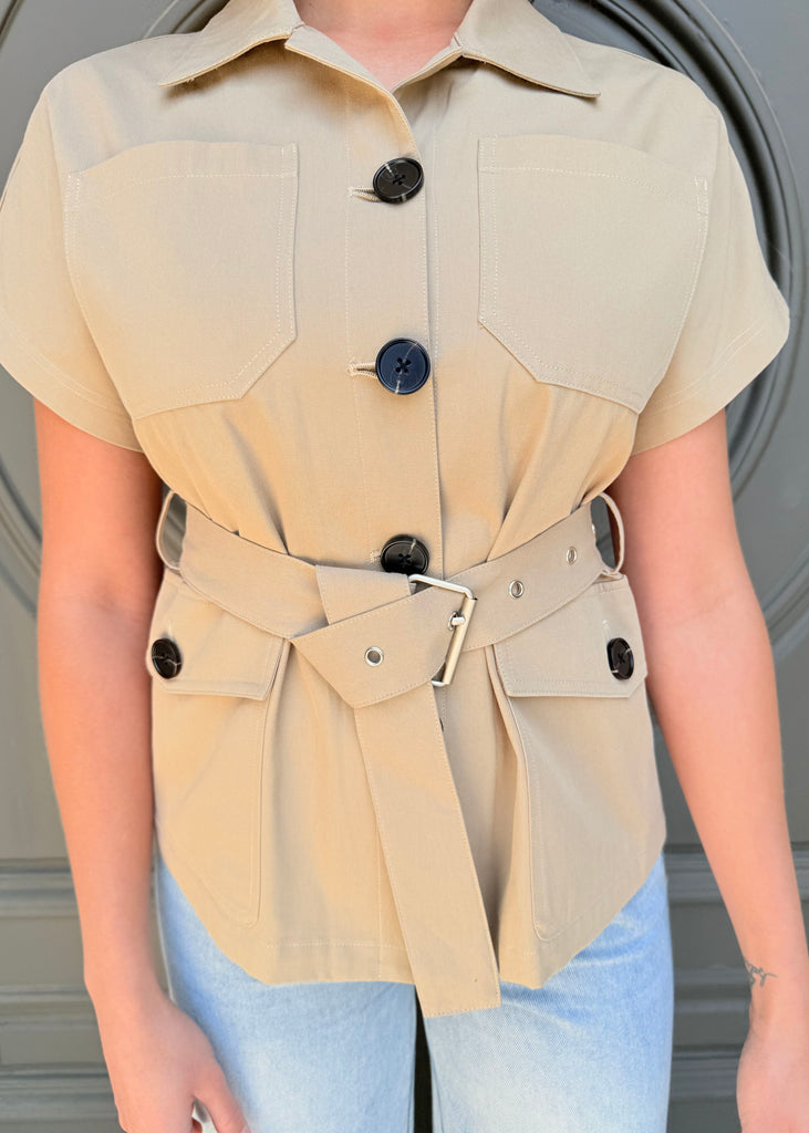 Beige short-sleeve shirt with black buttons and a belt worn by a person against a neutral background