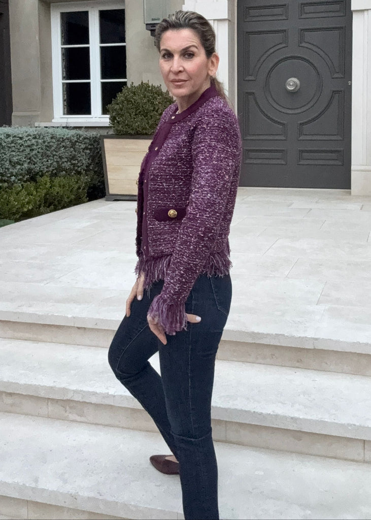 Woman in a purple jacket standing in front of a large house with a gray door.