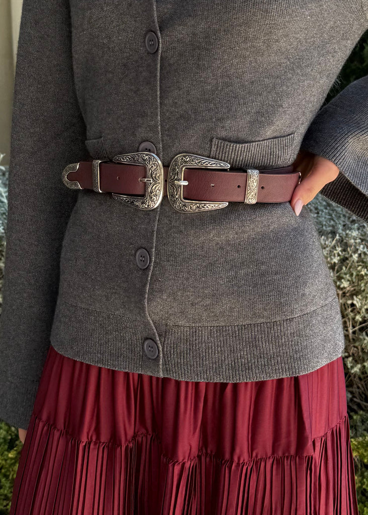 Woman wearing a gray sweater and red skirt standing outdoors.