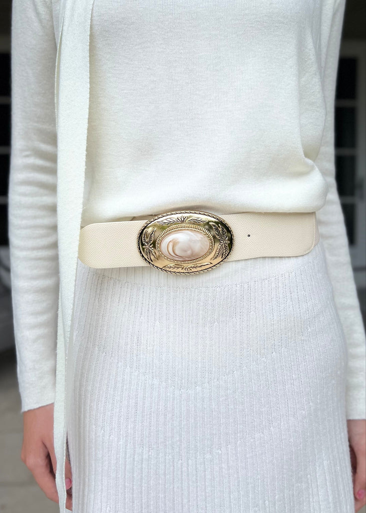 Person wearing a white outfit with a decorative belt outdoors.