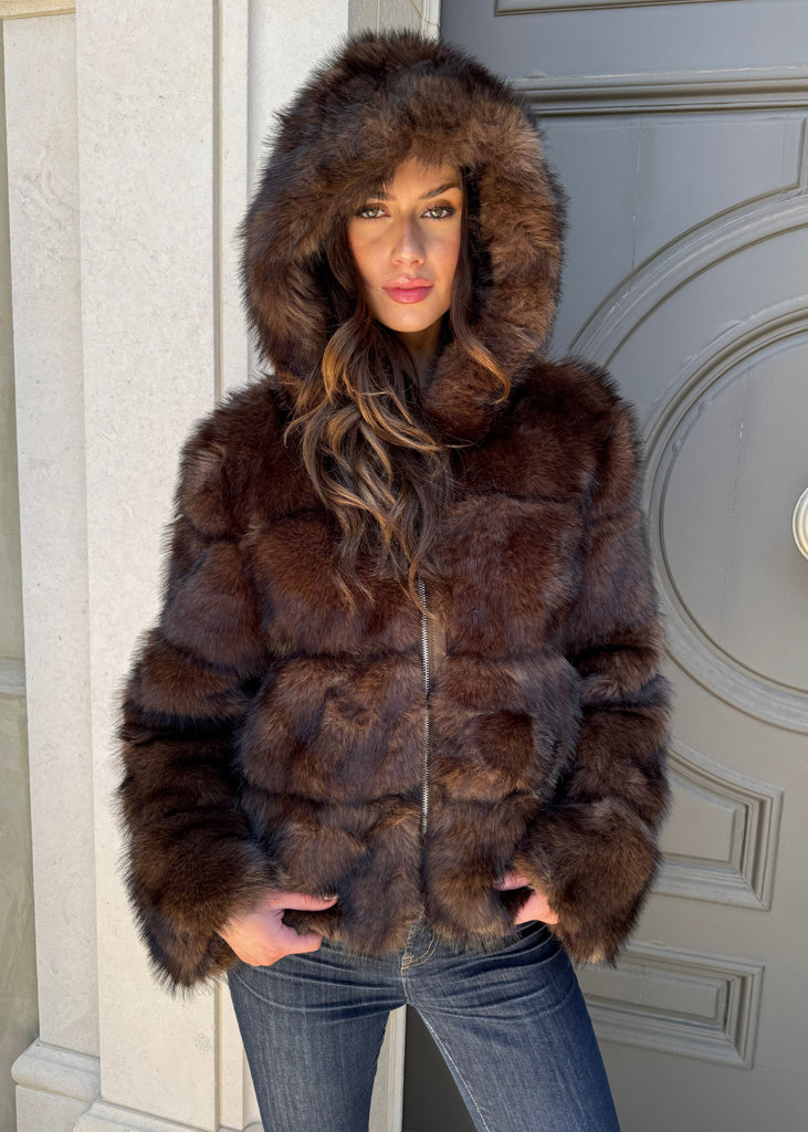 Woman wearing a brown fur coat standing in front of a door.