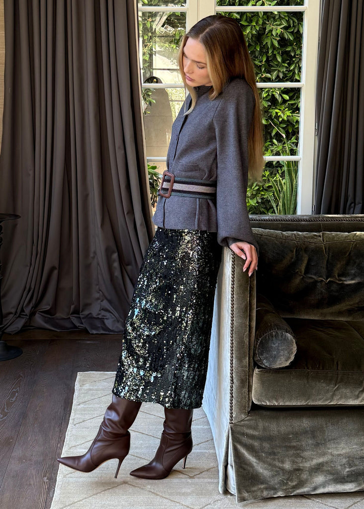 Woman standing in a stylish living room with a green sofa and large windows.