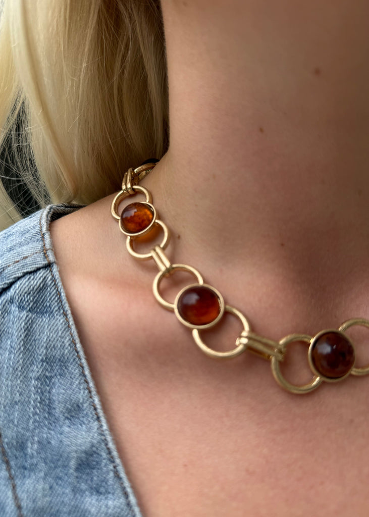 Gold necklace with amber-colored stones worn by a person with blonde hair and denim jacket.
